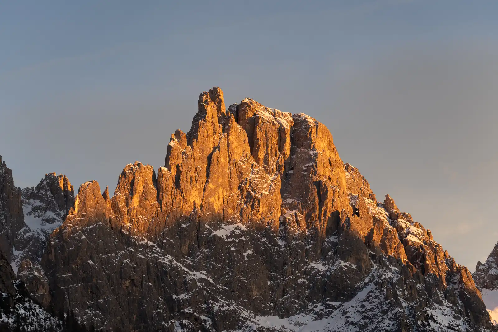 Vista di una montagna illuminata dal sole al tramonto con neve sulle cime.