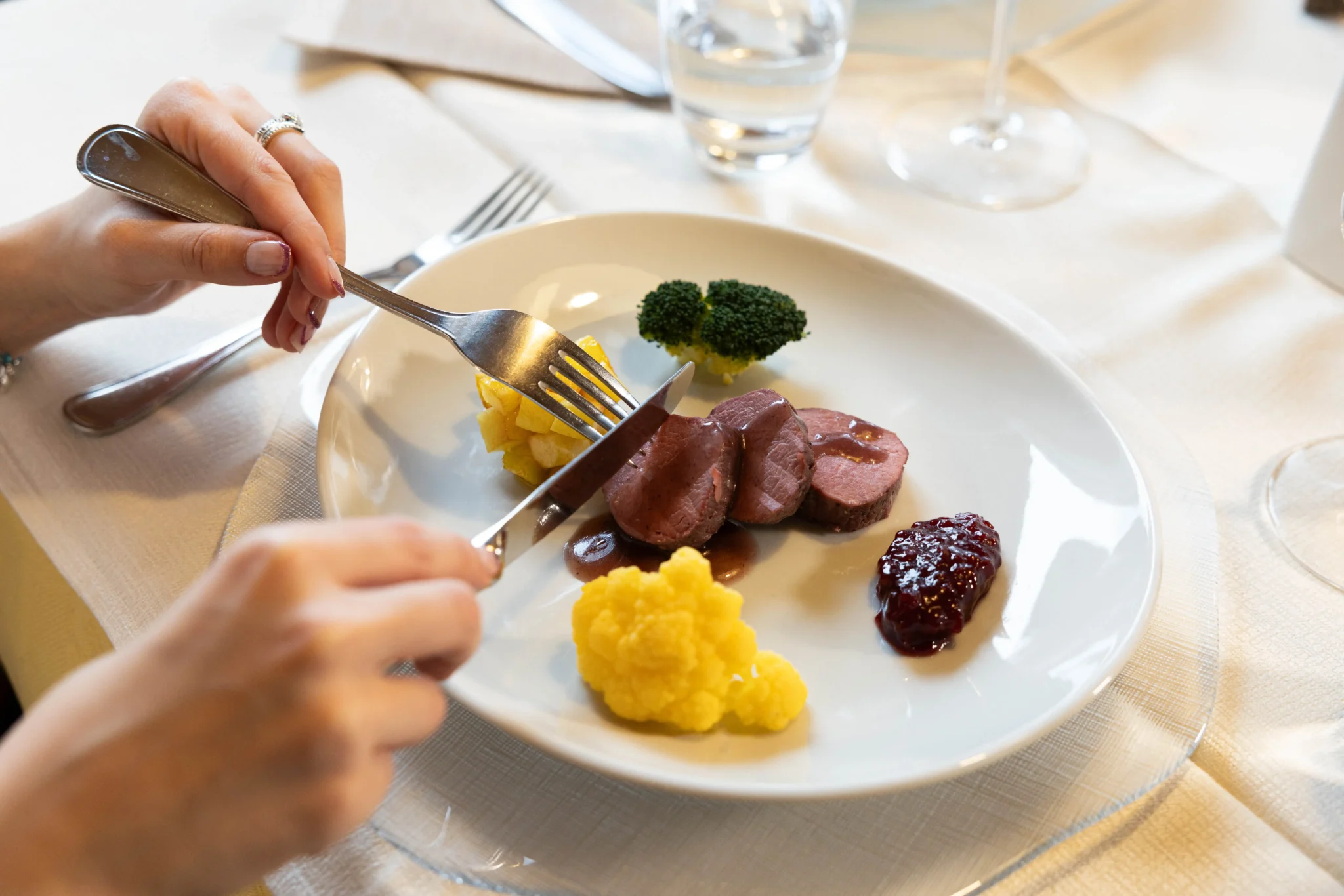 Piatto gourmet con carne, broccoli, patate e salsa di frutti di bosco, servito in un ristorante elegante.