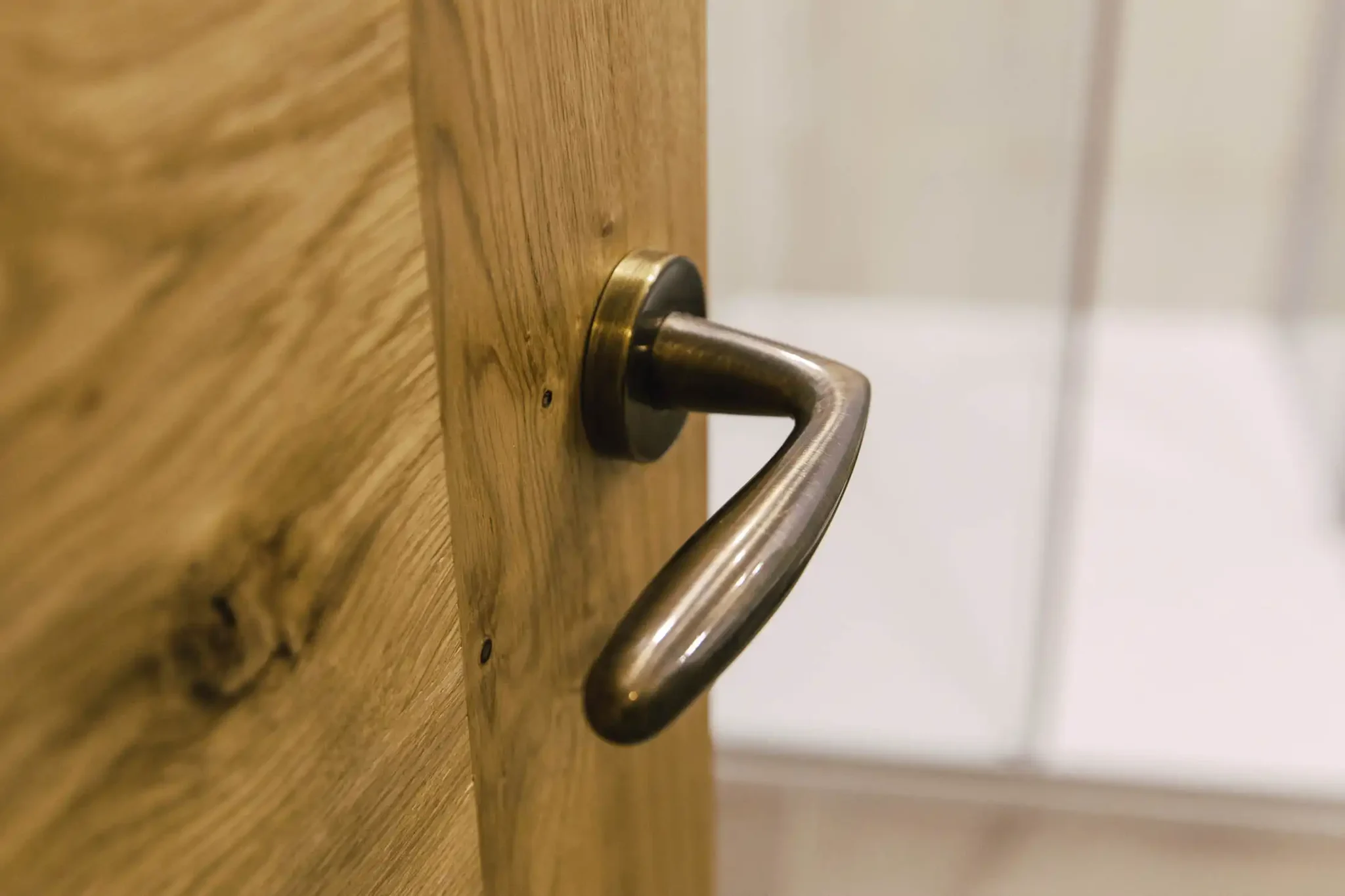 Maniglia metallica su una porta di legno chiaro.