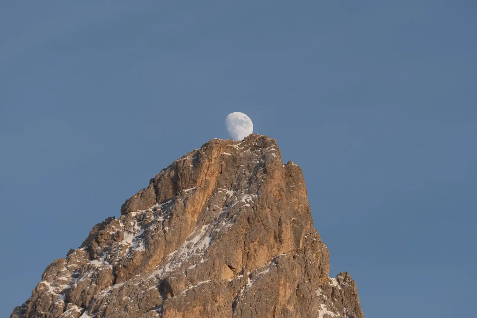 La luna sorge dietro una cima montuosa innevata contro un cielo blu.