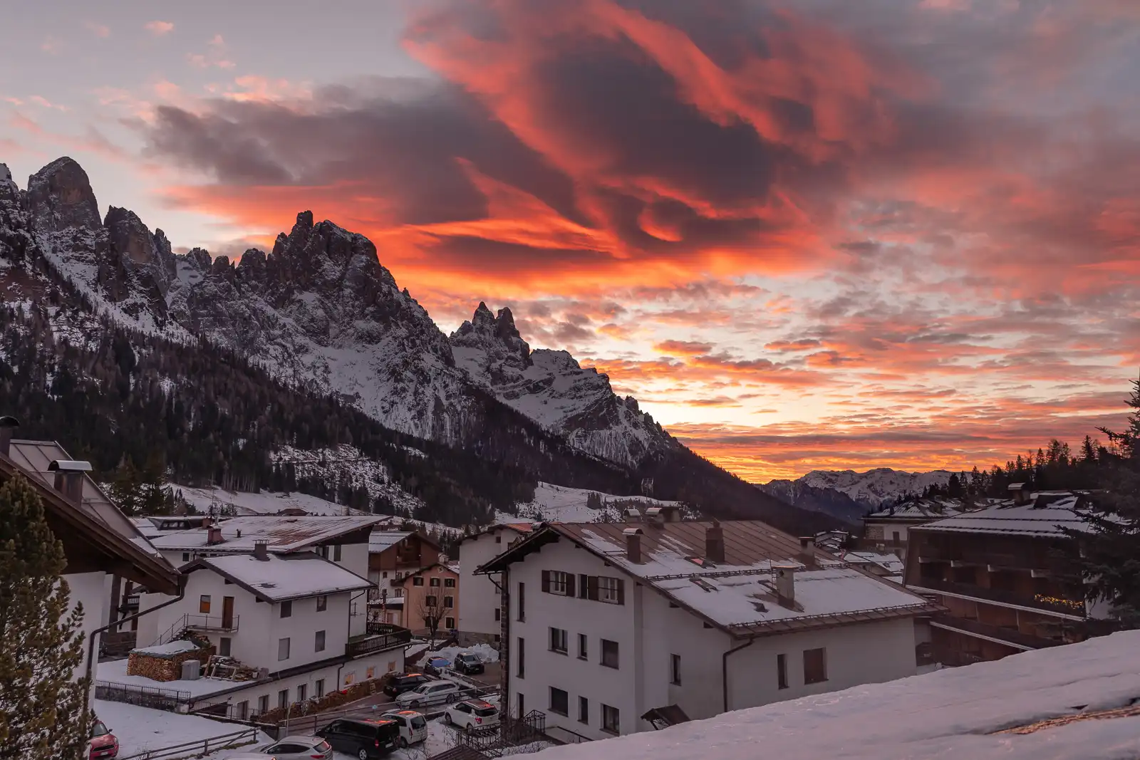 Tramonto arancione sopra un villaggio di montagna innevato con montagne sullo sfondo.