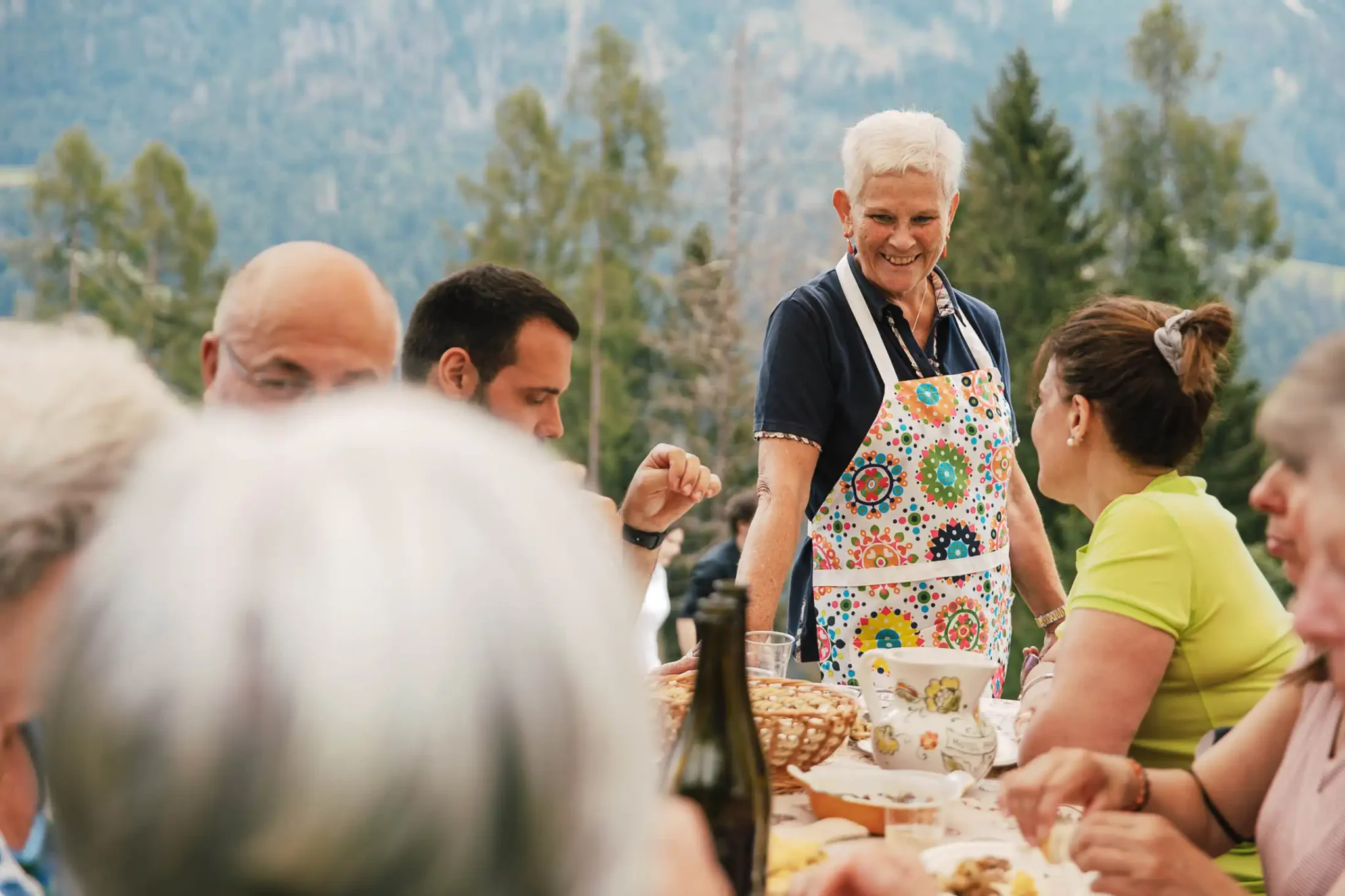 Gruppo di persone che condividono un pasto all'aperto con vista sulle montagne.