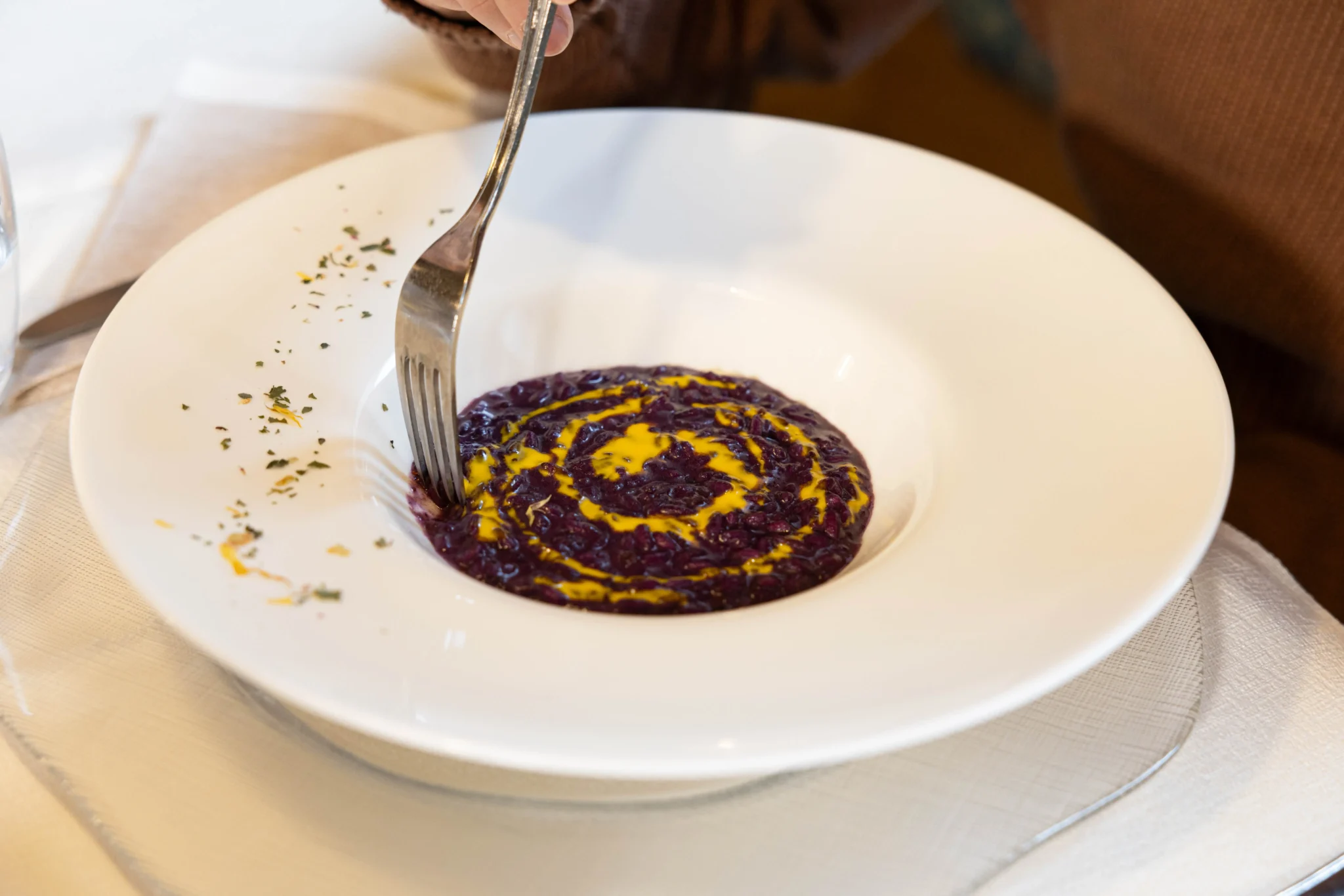 Risotto al vino rosso decorato con crema gialla in un piatto bianco.