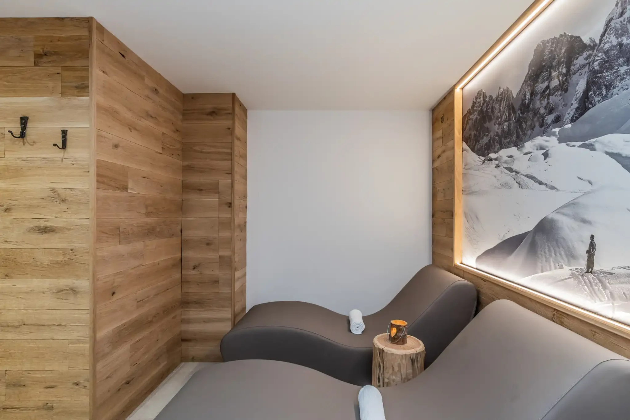 Sala relax con sedie ergonomiche e pareti in legno, illuminata da un grande pannello fotografico di montagna.