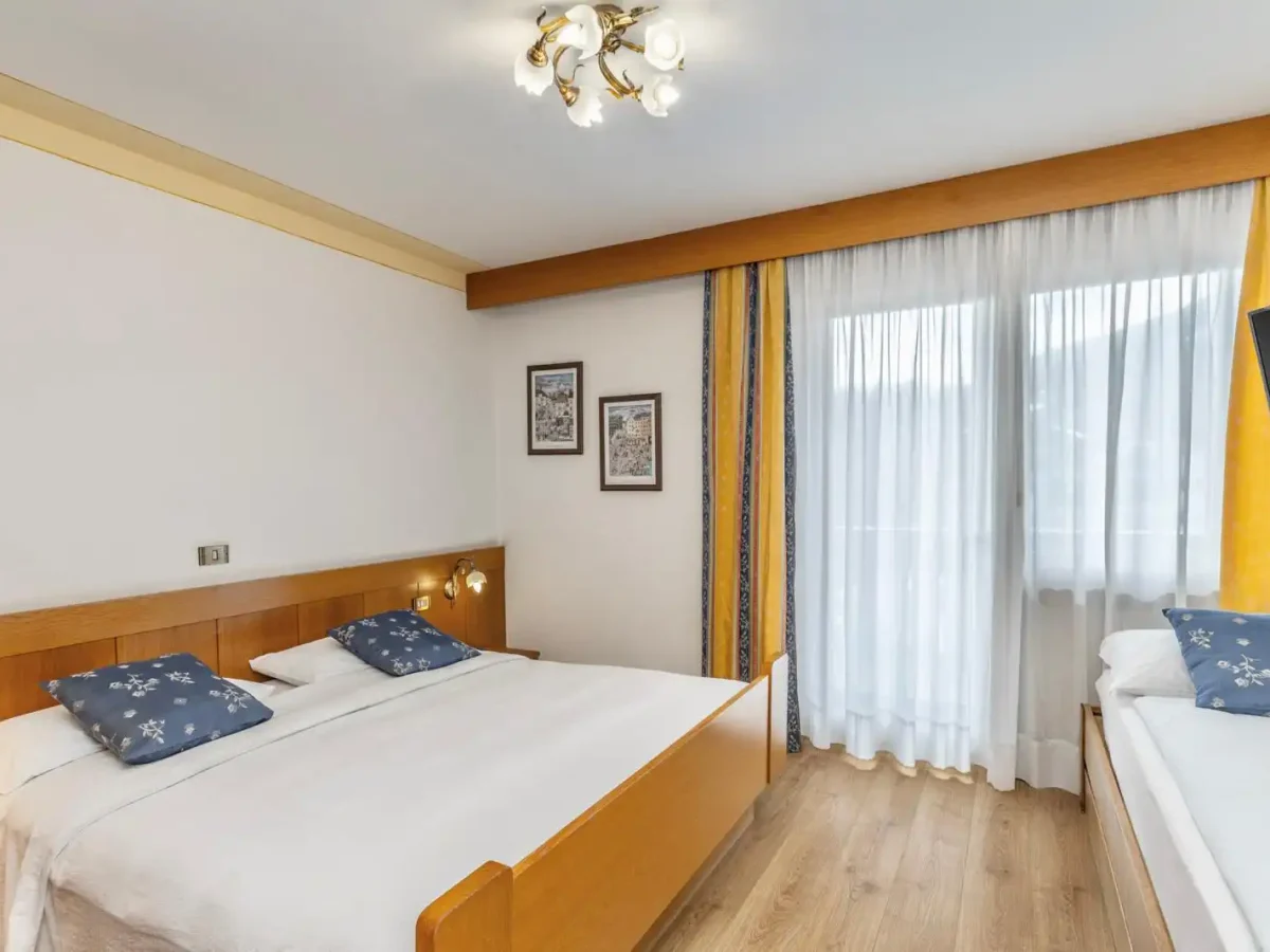 Camera da letto luminosa con arredamento in legno, letto matrimoniale e singolo, e tende gialle.