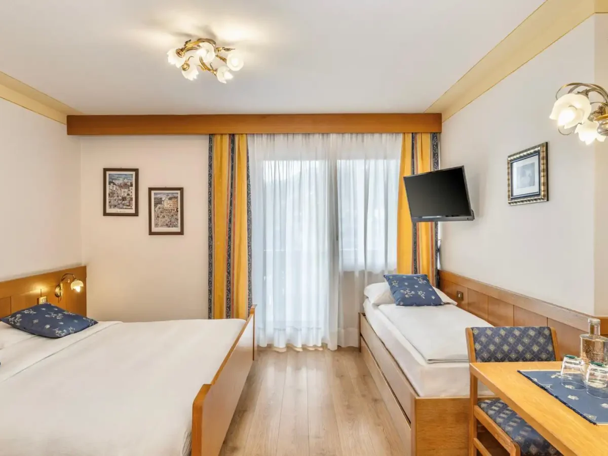 Camera d'albergo accogliente con due letti, televisore a parete e tavolino vicino alla finestra con tende gialle.