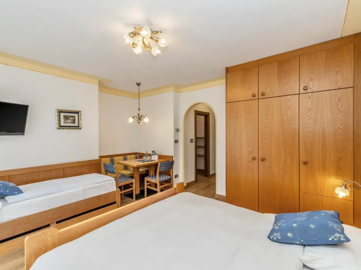 Camera d'albergo accogliente con letti singoli, armadio in legno, tavolo con sedie e TV a parete.