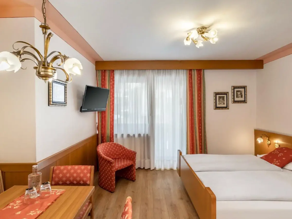 Camera d'albergo accogliente con letti matrimoniali, tavolo, sedie e TV a schermo piatto.