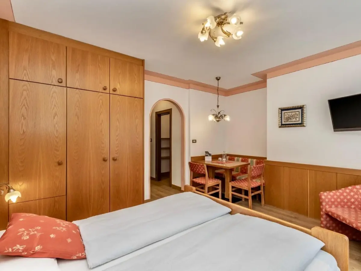 Camera d'albergo accogliente con letto matrimoniale, armadio in legno, zona pranzo e televisione.