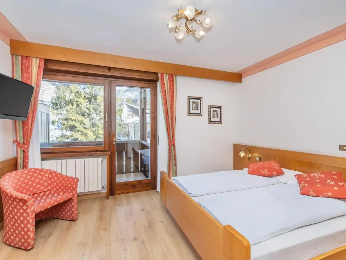 Camera da letto accogliente con arredi in legno, finestra panoramica e decorazioni rosse.
