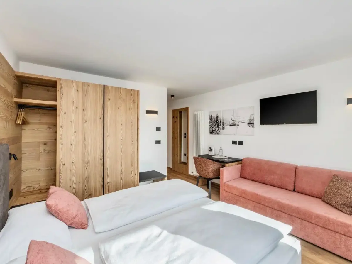 Camera d'albergo moderna con letti, armadio in legno, divano rosa e TV a schermo piatto.