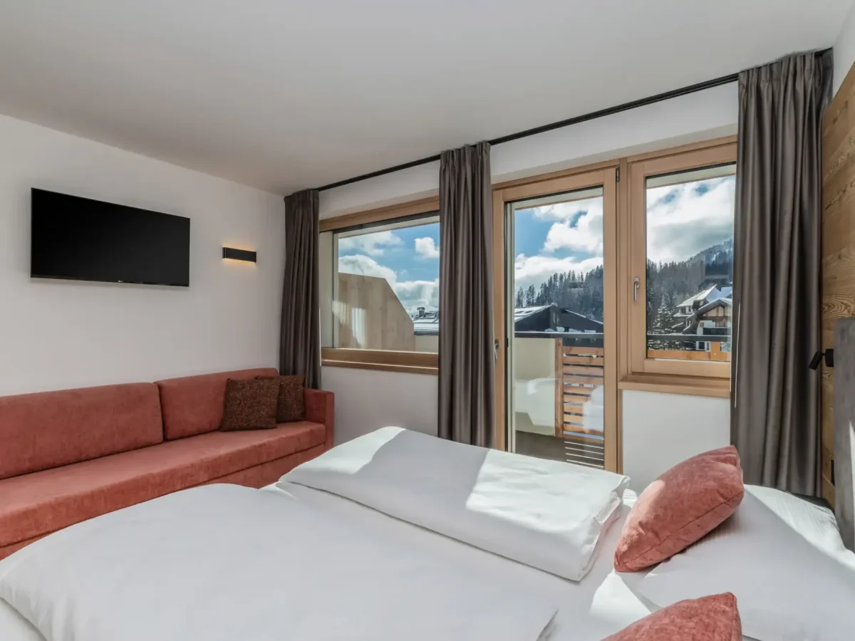Camera d'albergo luminosa con vista panoramica dalla finestra su paesaggio montano innevato.