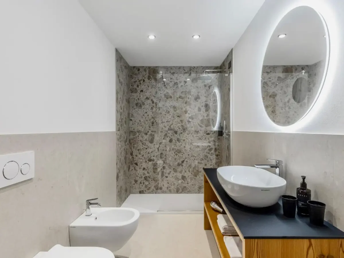 Bagno moderno con doccia, bidet, lavabo su mobile in legno e specchio illuminato.