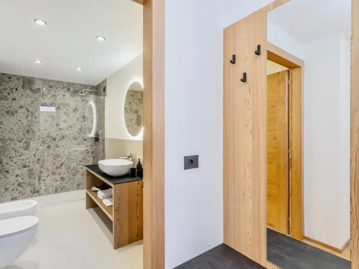 Bagno moderno con doccia in vetro, specchio retroilluminato e arredamento in legno.