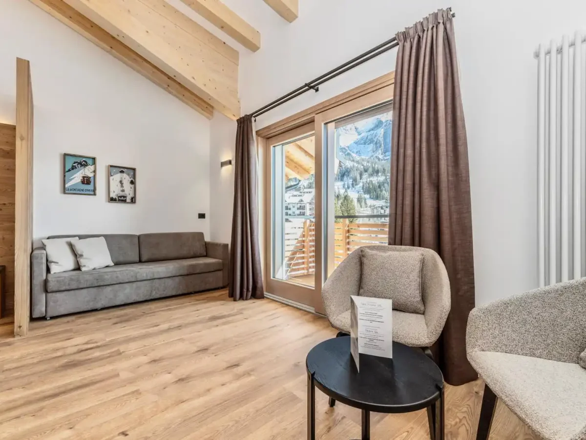 Soggiorno moderno con soffitto in legno, divano grigio e vista sulle montagne innevate.