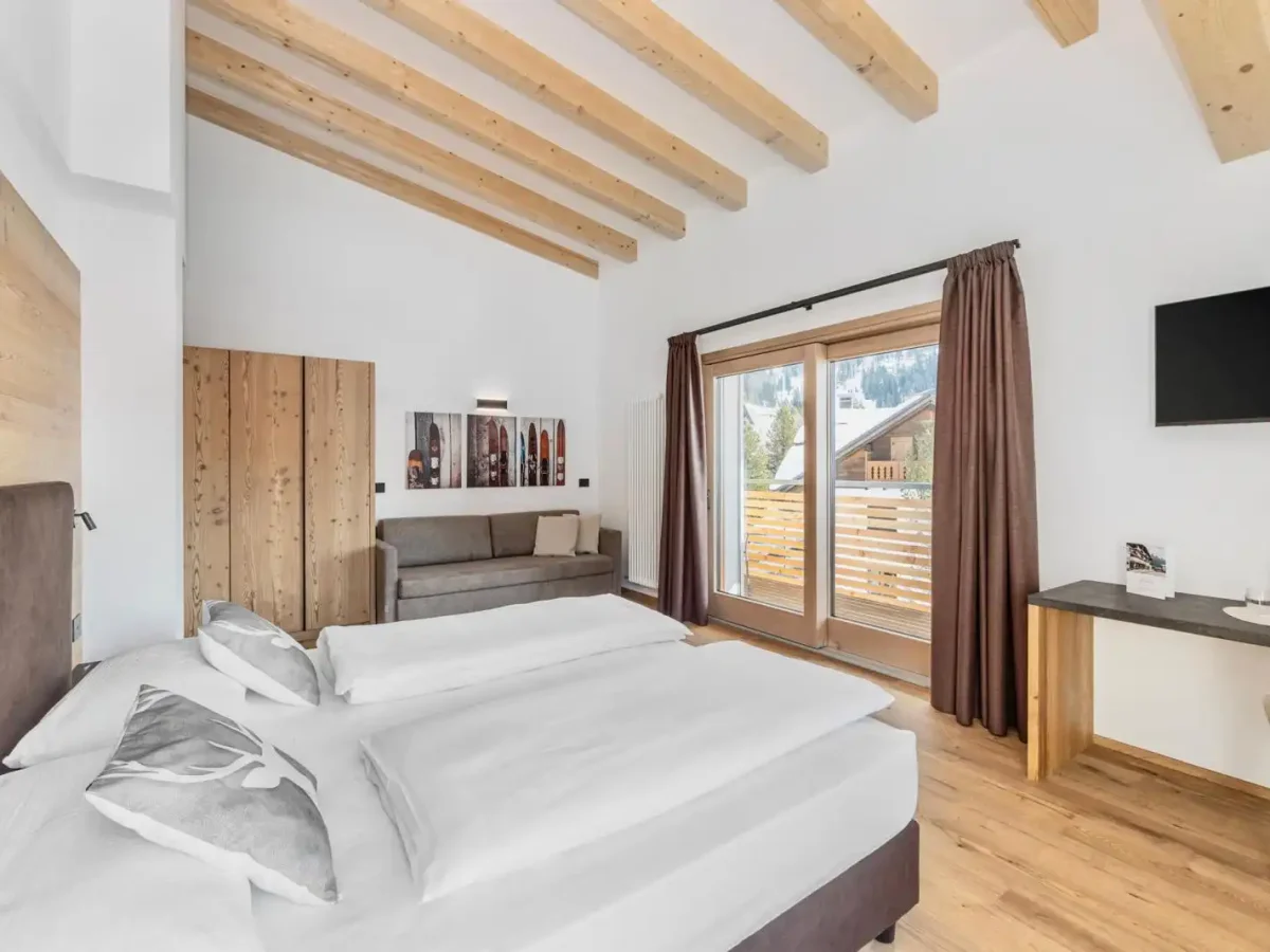 Camera da letto moderna con soffitto in legno, ampio letto, divano, scrivania e vista su un balcone.
