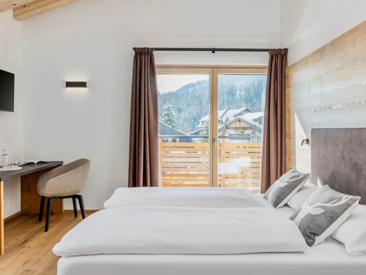 Camera d'albergo moderna con balcone affacciato su montagne innevate.