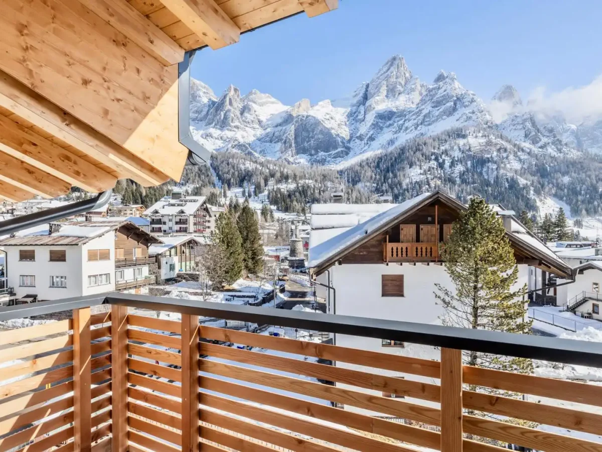 Vista di un villaggio alpino innevato con montagne sullo sfondo, vista da un balcone in legno.