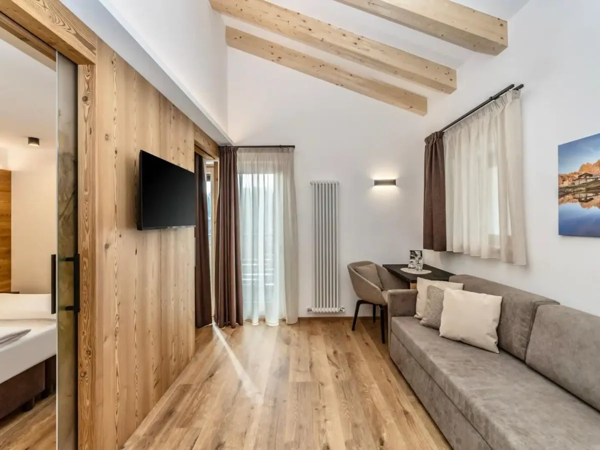 Camera moderna con pavimenti in legno, soffitto con travi a vista e arredi eleganti.