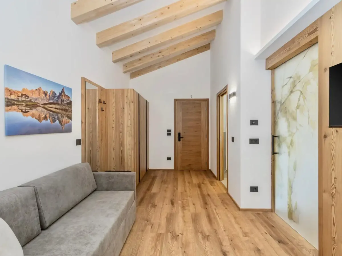Camera moderna con arredamento in legno, soffitto con travi a vista e divano grigio.