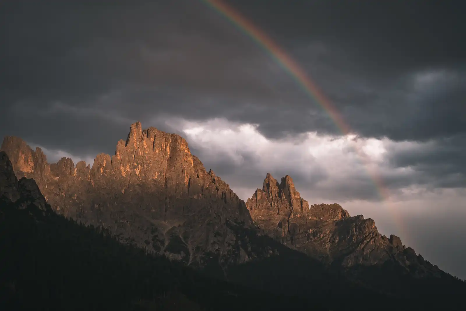 Montagne al tramonto con un arcobaleno sotto un cielo nuvoloso.